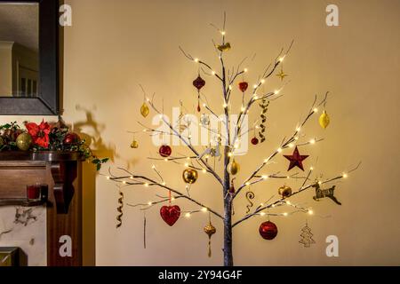 Moderno albero di Natale in stile Twig decorato con tradizionali decorazioni natalizie rosse e dorate con effetto neve e legature Foto Stock