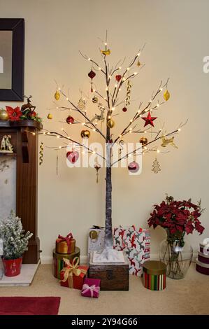 Moderno albero di Natale in stile Twig decorato con tradizionali decorazioni natalizie rosse e dorate con effetto neve e legature Foto Stock