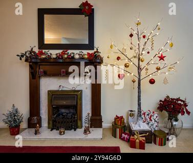 Moderno albero di Natale in stile Twig decorato con tradizionali decorazioni natalizie rosse e dorate accanto al caminetto decorato nell'area lounge Foto Stock