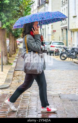 Donna con ombrello che parla al telefono cellulare e cammina lungo la strada del centro città sotto la pioggia battente - Tours, Indre-et-Loire (37), Francia. Foto Stock