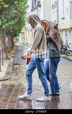 Coppia che cammina lungo la strada della città sotto la pioggia battente senza ombrello - Tours, Indre-et-Loire (37), Francia. Foto Stock