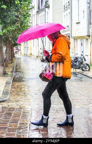 Donna con ombrello rosa che cammina lungo la strada del centro città sotto la pioggia battente - Tours, Indre-et-Loire (37), Francia. Foto Stock