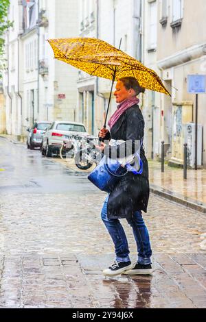 Donna con ombrello danneggiato che cammina lungo la strada del centro città sotto la pioggia battente - Tours, Indre-et-Loire (37), Francia. Foto Stock