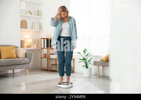 Menopausa, aumento di peso. Donna preoccupata in piedi su bilance da pavimento a casa Foto Stock