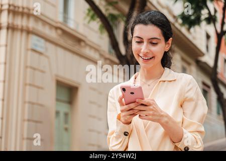 Ritratto con una copia di una giovane donna sorridente che usa un cellulare all'aperto, in piedi in un'area urbana mentre interagisce con il suo smartphone, concentrata e impegnata, godendosi una giornata informale all'aperto. Foto di alta qualità Foto Stock