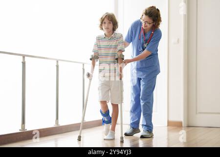 Bambino ferito alle stampelle. Ragazzo in cast su piede e gamba. Ragazzino con le ancore spruzzate che imparano a camminare di nuovo. Fisioterapia in clinica sanitaria. Foto Stock