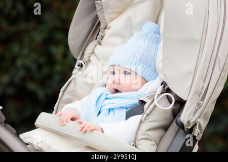 Bambino nel passeggino. Bambino in carrozza in inverno. Abbigliamento caldo per passeggiate attive con il bambino durante la stagione fredda. Simpatico ragazzino con cappello e giacca a maglia Foto Stock