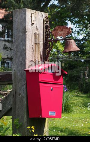 Vista ravvicinata di una cassetta di lettere rossa chiusa montata su un palo di legno con campana e maiale in metallo sopra fuori da una casa di campagna, Norfolk, Inghilterra, Regno Unito Foto Stock