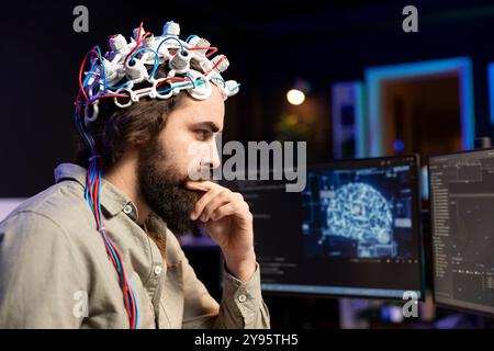 Programmatore che utilizza le cuffie EEG per caricare la sua mente nel computer, ottenendo l'immortalità. Neuroscienziato in appartamento che sperimenta il trasferimento di coscienza nel ciberspazio Foto Stock