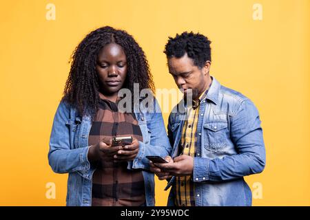 Gli afroamericani in una relazione scrivono messaggi sui loro telefoni, passano insieme davanti alla telecamera. Giovane coppia sposata che mostra a vicenda divertenti video su smartphone. Foto Stock