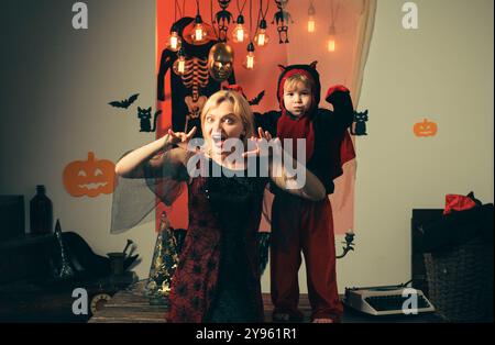 Madre che indossa come strega, figlio che indossa come diavolo. Ragazzo in costume diavolo. Bella giovane donna con un bambino con zucche autunno. Madre e figlio sorridenti Foto Stock