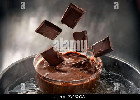 Pezzi di cioccolato che cadono in una ciotola di vetro in un bagno d'acqua per la fusione, lo spazio di copia, la messa a fuoco selezionata, la profondità di campo stretta Foto Stock