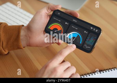 Uomo che monitora le letture del contatore intelligente sul telefono cellulare a tavola, primo piano Foto Stock