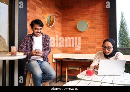 Due giovani lavoratori asiatici, che discutono al tavolino del caffè, che lavorano con un notebook spiegando il file sullo schermo Foto Stock
