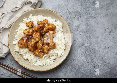 Pollo cinese agrodolce con semi di sesamo e riso su piatto di ceramica con bacchette vista dall'alto su fondo in pietra rustica grigia, traditiona Foto Stock