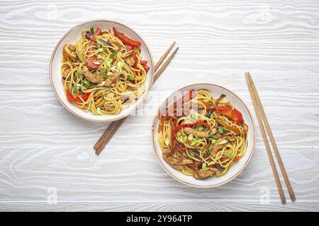 Due ciotole con Chow Mein o lo Mein, tradizionali spaghetti cinesi con carne e verdure, serviti con bacchette e vista dall'alto su bianco rustico Foto Stock