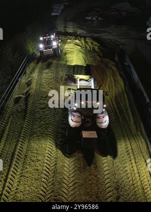 Due trattori che lavorano di notte con i fari accesi in un campo rurale, raccolta del mais, Dachtel, Foresta Nera, Germania, Europa Foto Stock