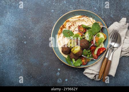 Pasto arabo medio orientale con falafel fritto, hummus, insalata di verdure con coriandolo verde fresco e foglie di menta in ciotola di ceramica su fondo rustico di pietra Foto Stock