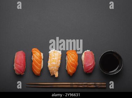 Vista dall'alto del tradizionale sushi giapponese con salsa di soia e bacchette su sfondo nero scuro minimale. Sushi con salmone, tonno e gamberi, spazio per il testo Foto Stock