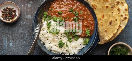 Tradizionale piatto punjabi indiano dal makhani con lenticchie e fagioli in ciotola nera servito con riso basmati, naan flat bread, coriandolo fresco e cucchiaio Foto Stock