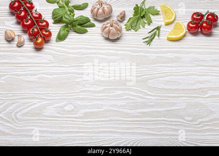 Composizione sana degli ingredienti alimentari con pomodori ciliegini freschi, erbe, spicchi d'aglio, spicchi di limone su fondo rustico in legno bianco, colpo d'aria sospeso W Foto Stock