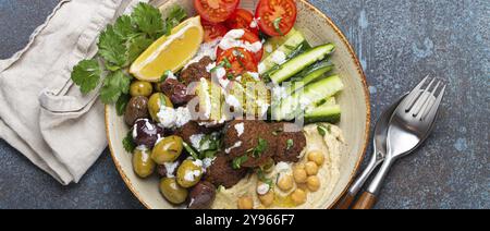 Insalata di falafel con hummus, verdure, olive, erbe aromatiche e salsa di yogurt. Pranzo vegano con vista dall'alto su sfondo rustico in pietra, pasto salutare con piatti Foto Stock