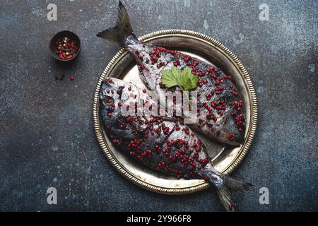 Due pesci crudi dorado conditi in pepe rosa pronto per essere cucinato su piatto rustico di metallo vista dall'alto. Cucina sana, dieta alimentare mangiare concetto. Foto Stock