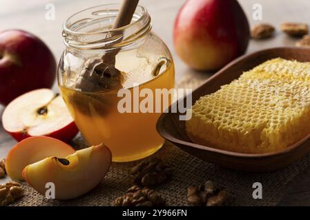 Barattolo con miele, cucchiaia di miele, favo, mele rosse e noci sul tavolo della cucina, fotografia di cibo, fotografia di cibo Foto Stock