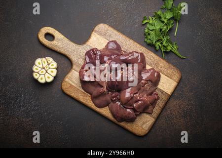 Fegato di pollo crudo su tagliere di legno vista dall'alto su un tavolo da cucina rustico scuro con fondo in cemento con prezzemolo e aglio. Ingrediente alimentare sano, Foto Stock