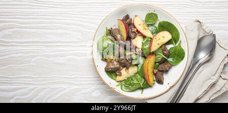Insalata sana con ingredienti ricchi di ferro fegato di pollo, mele, spinaci freschi e noci su piatto di ceramica bianca, sfondo di legno bianco dall'alto Foto Stock