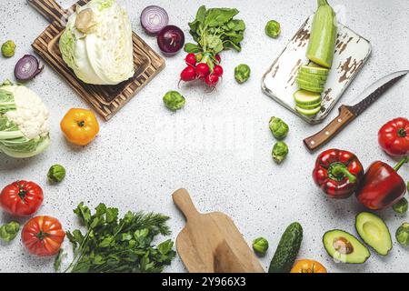 Verdure fresche varie con taglieri in legno e coltello sul tavolo da cucina bianco vista dall'alto. Cucina vegetariana con ingredienti sani, dieta Foto Stock