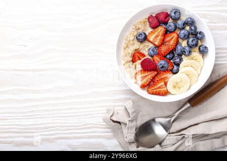 Porridge d'avena con frutta e frutti di bosco in ciotola con cucchiaio su sfondo bianco tavolo vista dall'alto, in casa sana colazione cereali con fragole Foto Stock