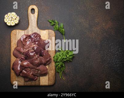 Fegato di pollo crudo su tagliere di legno vista dall'alto su un tavolo da cucina rustico scuro con fondo in cemento. Ingrediente alimentare sano, fonte di ferro, folato, Foto Stock