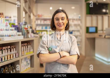 Orgogliosa giovane farmacista in piedi con le braccia incrociate sorridente alla macchina fotografica nel negozio Foto Stock