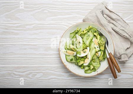 Sana ciotola per insalata di avocado verde con uova sode, cetrioli a fette, fagioli edamame, olio d'oliva ed erbe aromatiche su piastra in ceramica vista dall'alto su ruggine di legno bianca Foto Stock