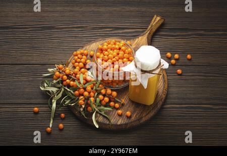 Spinoso marino bevanda sana in bottiglia, bacche mature in vaso di vetro e rami con foglie vista dall'alto su sfondo rustico di legno scuro, ottimo per la pelle, h Foto Stock