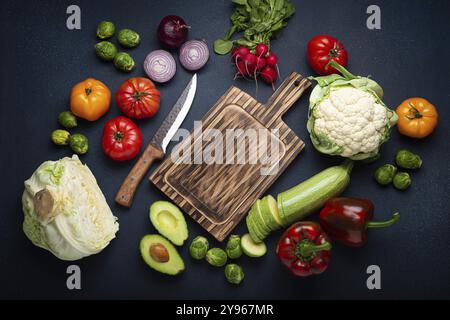 Verdure fresche, zucchine tagliate, tagliere di legno e coltello su sfondo rustico scuro vista dall'alto. Cucinare un pasto vegetariano da salutare ingred Foto Stock