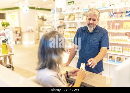 Vista posteriore di una farmacista matura che assiste un cliente al banco Foto Stock