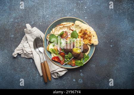 Pasto arabo mediorientale con falafel fritto, hummus, insalata di verdure con coriandolo verde fresco e foglie di menta, pita pane in ciotola di ceramica su pietra r Foto Stock