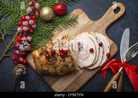 Prosciutto di Natale affettato con frutti di bosco rossi e decorazioni festose sul tagliere di legno, sfondo rustico scuro dall'alto. Natale e Capodanno Foto Stock