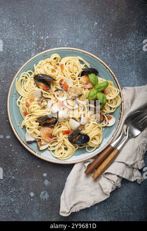 Spaghetti di pasta italiana di pesce con cozze, gamberetti, vongole in salsa di pomodoro con basilico verde sul piatto su fondo rustico in cemento blu sopra la testa. Io Foto Stock