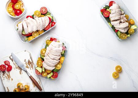 Sana preparazione del pasto per il pranzo, dieta filetto di pollo bollito con insalata di verdure in contenitori per il pranzo vista dall'alto sul tavolo da cucina in marmo bianco backgro Foto Stock