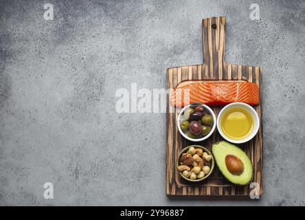 Fonti alimentari di grassi insaturi sani e omega 3: Filetto di salmone fresco crudo, avocado, olive, noci sul tagliere, pietra rustica sfondo vista dall'alto Foto Stock