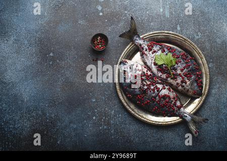 Due pesci crudi dorado conditi in pepe rosa pronto per essere cucinato su piatto rustico di metallo vista dall'alto. Cucina sana, dieta alimentare mangiare concetto. Foto Stock
