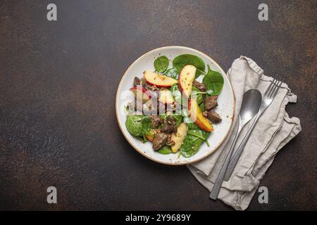 Insalata sana con ingredienti ricchi di ferro fegato di pollo, mele, spinaci freschi e noci su piatto di ceramica bianca, fondo di pietra rustica marrone scuro T. Foto Stock