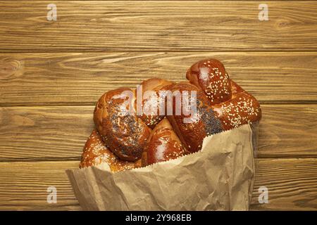 Pane Challah appena sfornato ricoperto di papavero e semi di sesamo in un sacchetto di carta, vista dall'alto su fondo rustico in legno, tradizionale cuisi festivo ebraico Foto Stock