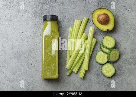 Bottiglia di frullato di verdure verdi con bastoncini di sedano fresco, avocado tagliato, cetriolo su sfondo grigio in cemento. Bevanda dietetica, nutrit sano Foto Stock