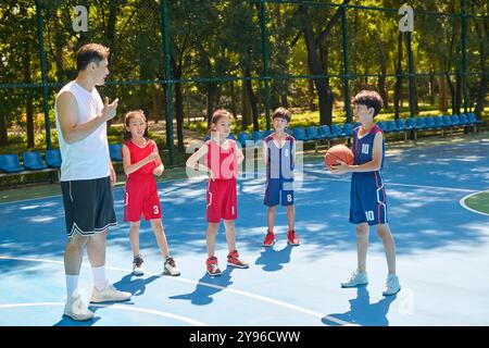 Coach che insegna ai bambini come giocare a basket Foto Stock
