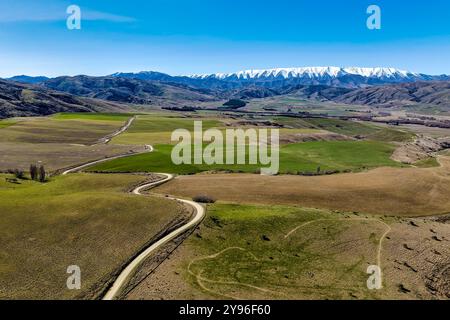 Strada di campagna tortuosa che attraversa campagna agricola vicino al passo alpino di Lindis Foto Stock