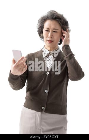Donna anziana che tiene in mano uno smartphone sembra confusa Foto Stock